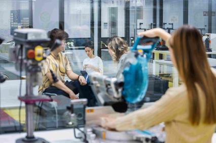 A group of people engaging in a discussion in a workshop environment with tools in the foreground.