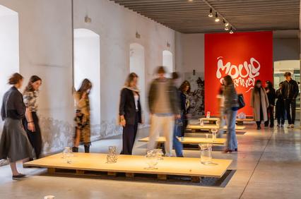 People viewing an art exhibition in a gallery with red and white walls and modern artwork installations.