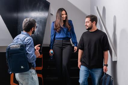 Three young adults engaging in conversation near a staircase.