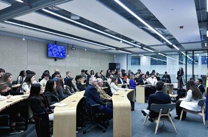 A large group of people seated in a modern conference room engaging in discussion.