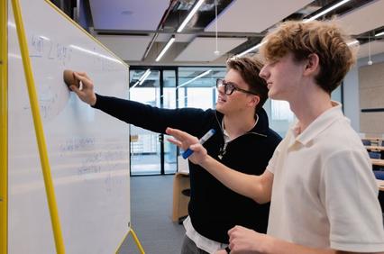 Two students collaborating at a whiteboard in a modern classroom.