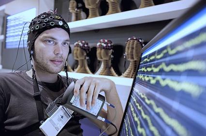 A man wearing an EEG cap observes brainwave readings on a monitor.