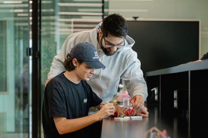 Two young men are collaborating on an electronic project at a desk.