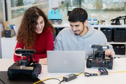 Two people are working together with robotic devices and a laptop in a bright, modern environment.