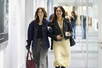 Two women walking and laughing together in a gallery with photographs on the walls.