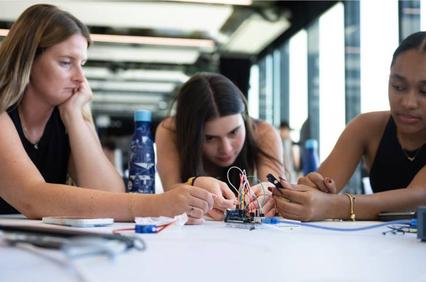 Three women are focused on a technical project involving electronics and wires.
