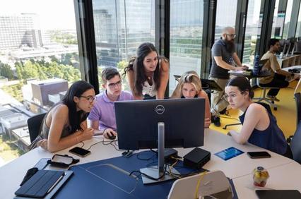 A group of young people collaborating around a computer in a modern office space.
