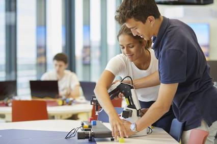 Two people are collaborating on a robotics project at a table in a bright, modern classroom.