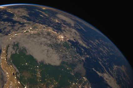 View of Earth from space showing continents and clouds illuminated by sunlight.