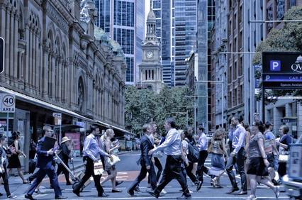 Group of businesspeople crossing a busy city street with modern buildings in the background.