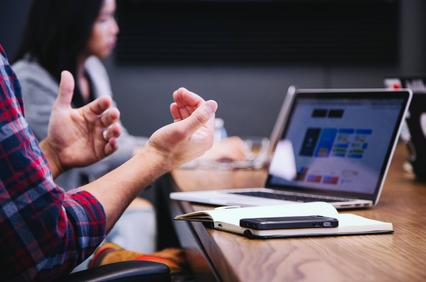 Computer in a table, hand os a person explaining information in a meeting.