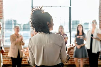 A woman is giving a presentation to a group of attentive colleagues in a brightly lit office space.
