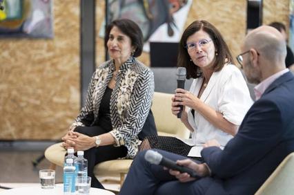 A woman speaks into a microphone during a panel discussion while seated next to other panelists.