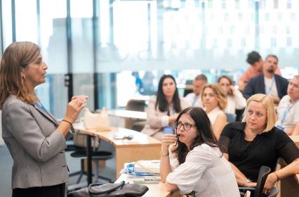 A woman is giving a presentation to a group of attentive listeners in a modern office environment.