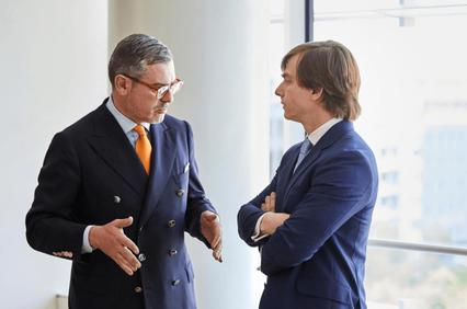 Two businessmen in suits are having a discussion inside an office building.