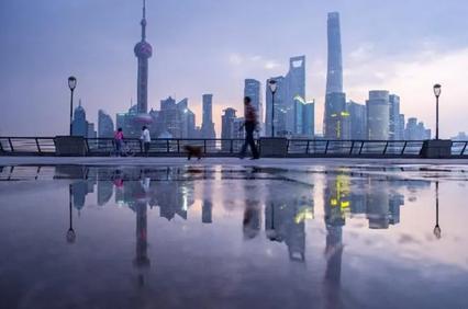 A misty evening in Shanghai with skyscrapers reflected in puddles.