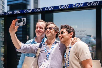 Three men are taking a selfie together in a sunny urban setting.