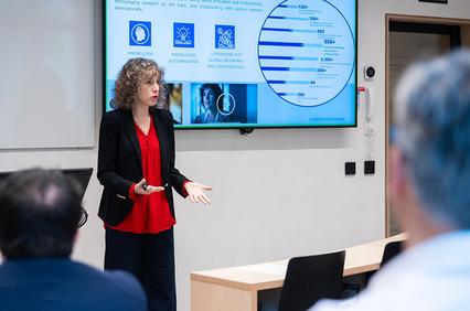 A woman in a red blouse presenting in front of a screen with data graphs during a seminar.