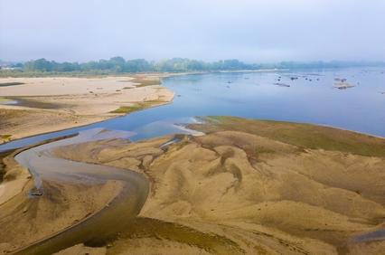 A serene river landscape with sandy shores and gentle curves of water under a misty sky.