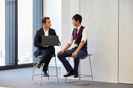 Two businessmen discussing over a laptop in a modern office setting.