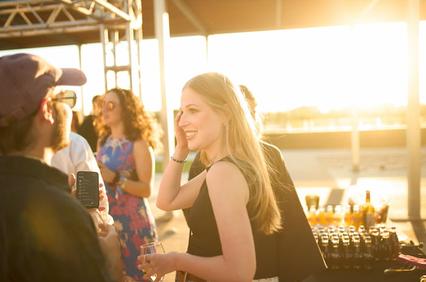 A woman smiling and engaging in a conversation at an outdoor party during sunset.