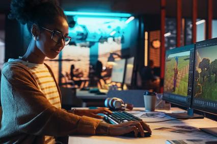 A woman is working on a computer in a modern office setup with multiple screens displaying vibrant graphics.