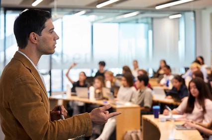 A man gives a lecture to a classroom full of engaged students.