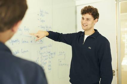 A person is presenting ideas on a whiteboard in an office setting.