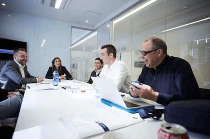 A group of professionals are seen engaging in a discussion around a conference table in a modern office setting.
