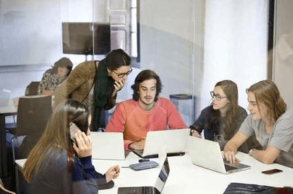 A group of young adults is engaged in discussion while using laptops at a modern office.