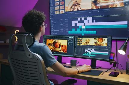 A person editing a video project on multiple computer screens in a dimly lit room.
