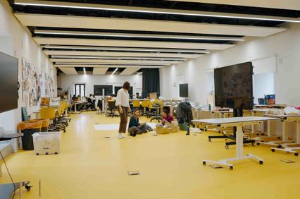 A spacious studio with yellow flooring and several people engaged in activities.