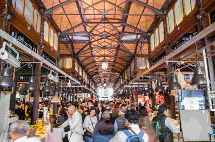 A bustling market hall filled with people and various food stalls.