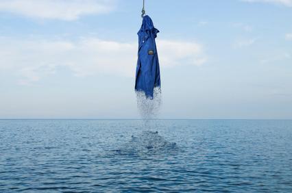 An umbrella hanging and dripping water above a calm sea.