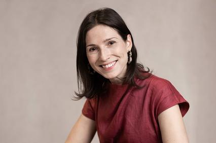 A woman with long dark hair smiling against a neutral background.