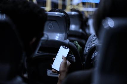 A person holding a smartphone in a dimly lit bus environment.