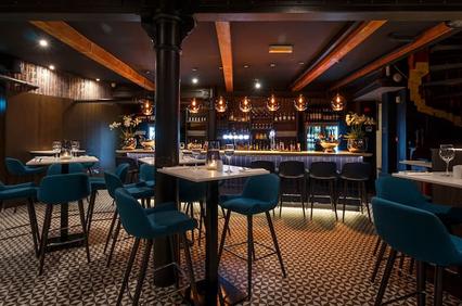 An elegant and modern restaurant interior featuring a bar with hanging lights and blue seating.