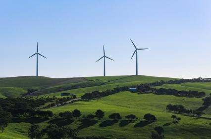 The image depicts a landscape with green hills and three wind turbines in the background under a clear blue sky.