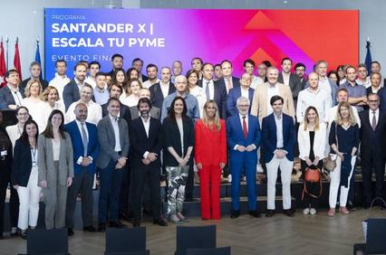 A large group of people posing for a photo at a business event with a Santander X banner in the background.