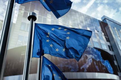 European Union flags fluttering in front of a modern building with a digital screen showing a map of Europe.