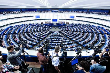 Photographers capturing a session at a modern, crowded parliamentary chamber with a blue and white color scheme.