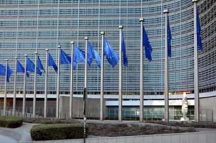 The image shows a modern building with multiple EU flags in front of it.
