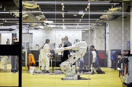 A robotic arm operates in a modern workspace where people collaborate on various projects.