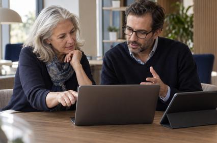 A man and a woman are collaborating over a laptop in a modern workspace.