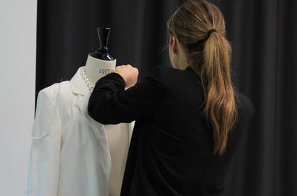 A person is adjusting a white blazer on a mannequin.
