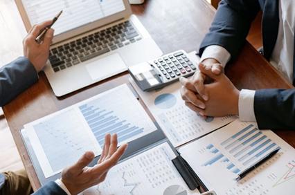Two professionals discussing financial data and charts at a desk with a laptop and calculator.