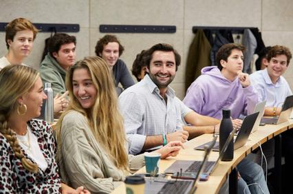 A group of students engaged in a classroom setting with laptops and casual interaction.