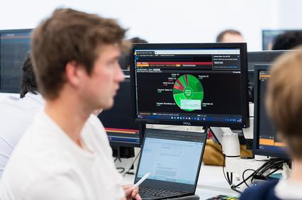 An office setting with two individuals focusing on computer screens displaying data visualizations.
