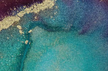 A close-up abstract image showing a vibrant blend of blue and gold pigments creating a textured, flowing pattern.