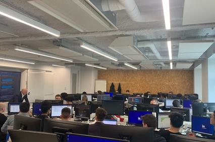 A modern office environment with numerous people working at computer desks.